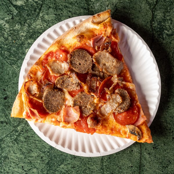 A slice of Pizza Nova's meat lover's pizza with pepperoni, sausage, and ham on a paper plate.