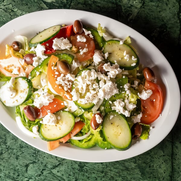 A vibrant Greek salad with cucumbers, tomatoes, olives, and feta cheese on a white plate.