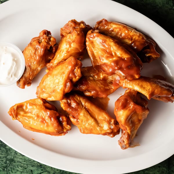 A white oval plate filled with saucy chicken wings and a small cup of dipping sauce.
