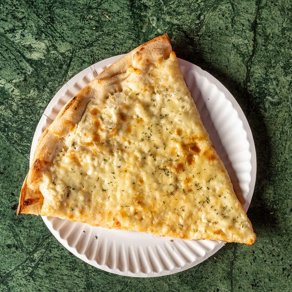 A slice of white pizza with herbs on a paper plate, against a green marble background.