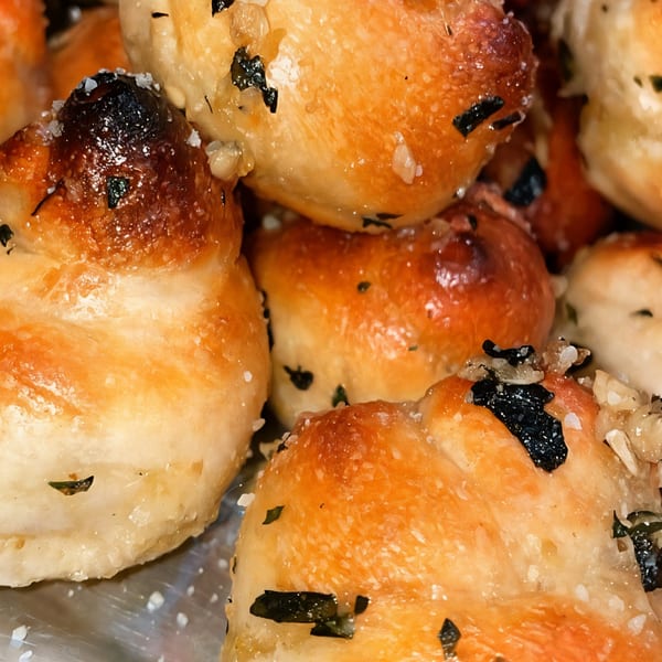 Close-up of golden-brown Pizza Nova garlic knots, sprinkled with herbs and coarse salt.
